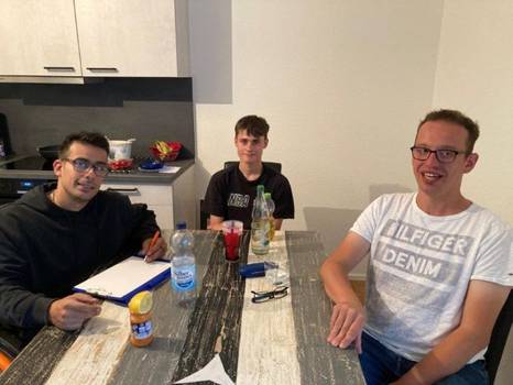 Drei Personen sitzen an einem Tisch und schauen Richtung Kamera. Drei Personen sitzen an einem Tisch und schauen Richtung Kamera.