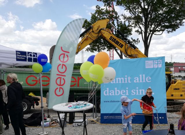 Impressionen von der Grundsteinlegung des „Quartier am Rotweg“ am 23.05.2025. Vor einem Banner der Diakonie Stetten spielen Kinder, eine erwachsene Person befindet sich im Gespräch. Impressionen von der Grundsteinlegung des „Quartier am Rotweg“ am 23.05.2025. Vor einem Banner der Diakonie Stetten spielen Kinder, eine erwachsene Person befindet sich im Gespräch.